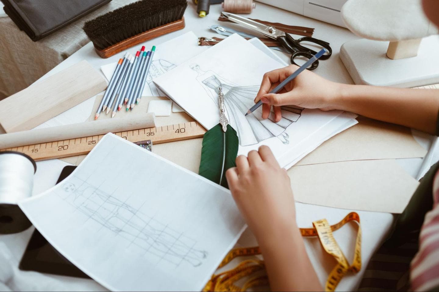 design a dress: Woman sketching a design on paper while surrounded by tools
