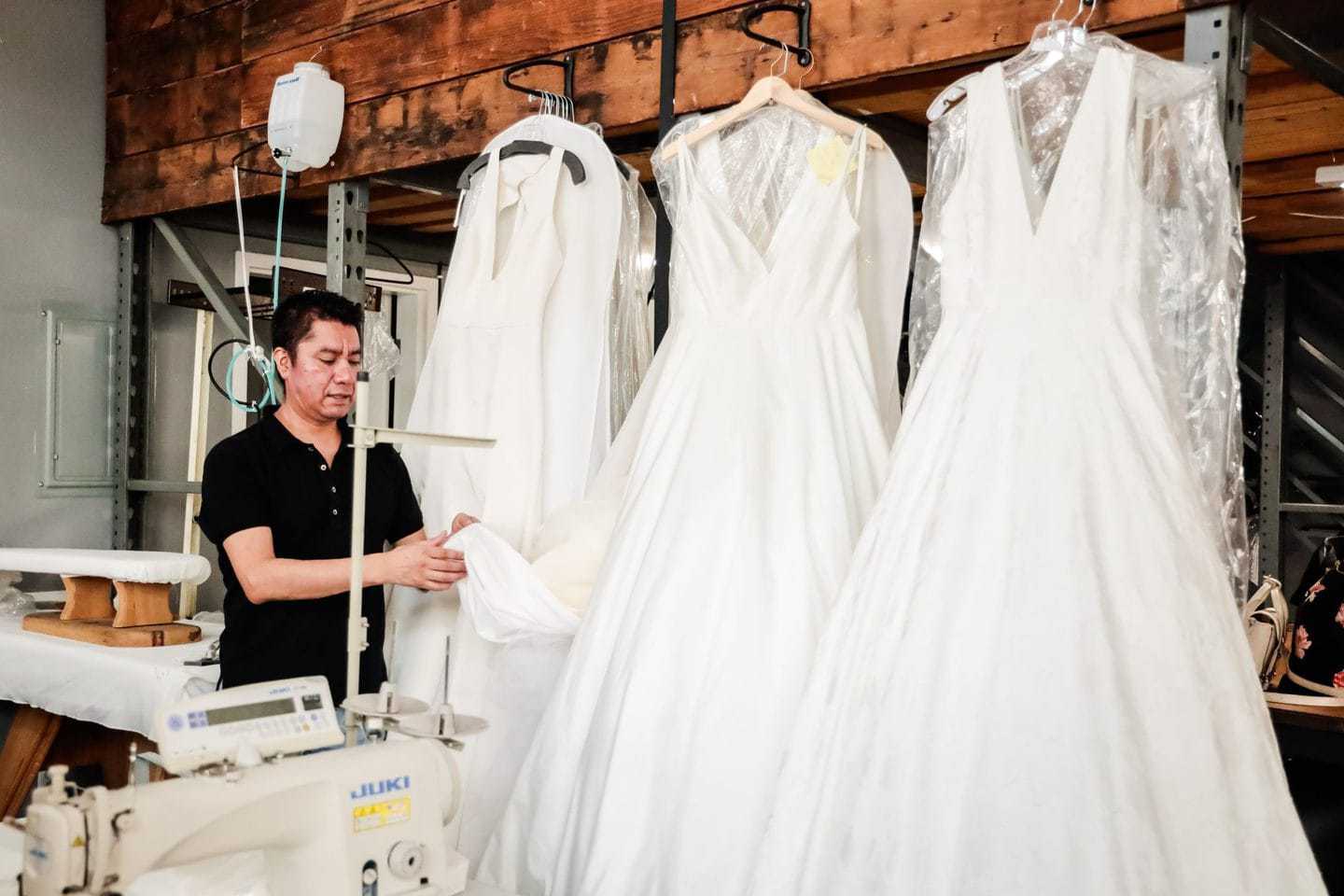 fashion line sheet: Designer examining wedding gowns inside a manufacturing studio